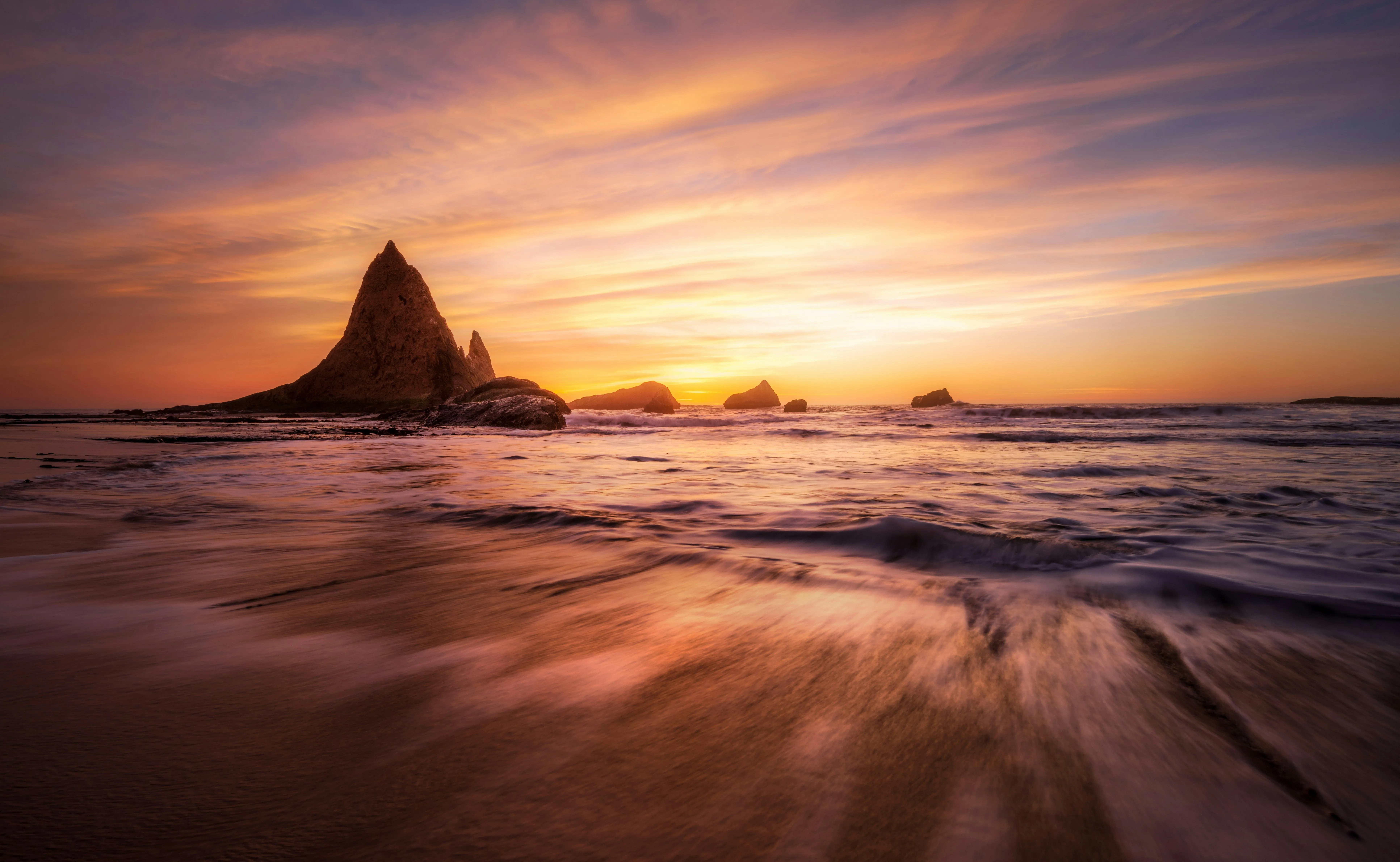 Rocks jutting out against the sky from the shore in a sunset beach photo